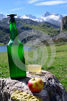 Green bottle and glass of natural Asturian cider made fromÂ fermented apples with view on Covadonga lake and tops of Picos de